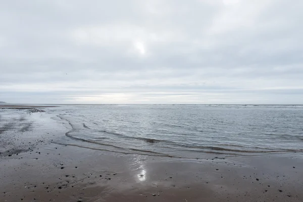 Avkopplande och mild lugnande vågor flyter in i en strand på en dyster mulen dag — Stockfoto