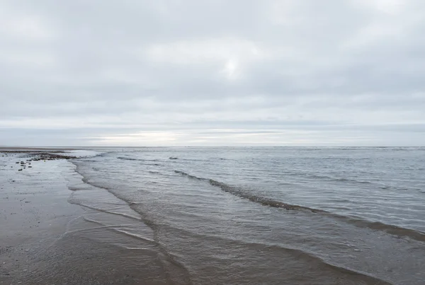 Ondas calmantes relaxantes e suaves que fluem para uma praia em um dia sombrio nublado — Fotografia de Stock