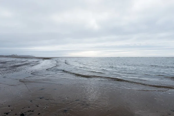 Ondas calmantes relaxantes e suaves que fluem para uma praia em um dia sombrio nublado — Fotografia de Stock