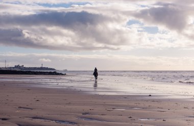 Mor bulutlu kumsalda gün batımında ücretsiz bir kadın binme silüeti