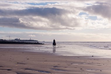 Mor bulutlu kumsalda gün batımında ücretsiz bir kadın binme silüeti