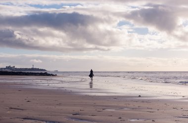 Mor bulutlu kumsalda gün batımında ücretsiz bir kadın binme silüeti