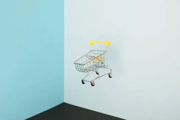 Schwebender Einkaufswagen auf blauem Hintergrund. Sicheres Online-Shopping auf Quarantäne-Konzept. Fliegender leerer Supermarkt-Einkaufswagen mit Kopierraum — Stockfoto