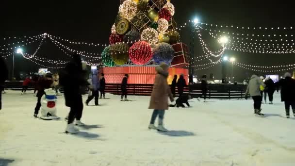사람들은 스케이트장에서 스케이트를 탄다. 크리스마스의 겨울 활동. 크리스마스 트리의 전구와 불빛. 옴스크, 러시아 연방 - 2020 년 12 월 22 일 — 비디오
