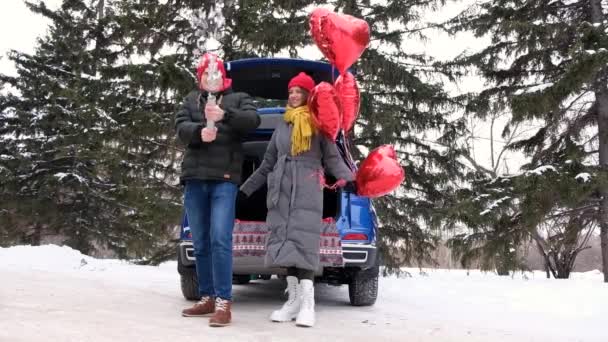 Αργή κίνηση ευτυχισμένο ζευγάρι σε κόκκινο καπέλο χαμογελώντας, γελώντας και γιορτάζοντας ρομαντική ημέρα του Αγίου Βαλεντίνου μαζί με κομφετί popper και κόκκινα μπαλόνια εξωτερική. Κόμμα κράκερ με πολύχρωμα κομφετί — Αρχείο Βίντεο