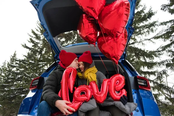 Portrait happy couple faces looking on at each other and laughing. Red heart shape balloons and word love. St Valentines Day celebration, romantic relationships, sincere feelings and love concept