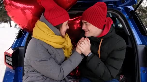 Porträt glückliches Paar. Freund wärmt sanft die Hände seiner Freundin und blickt in die Augen. Rote herzförmige Luftballons auf dem Hintergrund. Valentinstag-Feier, romantische Beziehungen, Liebeskonzept. — Stockvideo