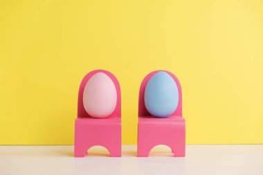 Paskalya tatili konsepti ve tatlı yumurtalar. Farklı duygular ve duygular. Sarı arka planda pembe sandalyelerde oturan sevimli çift yumurtaları.