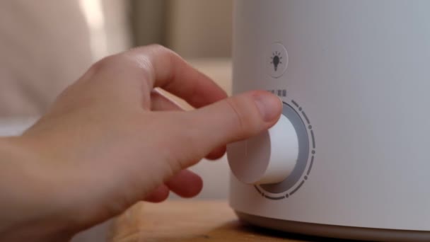 Mujer enciende el humidificador de aire moderno, difusor de aceite de aroma en casa. Mejorar la comodidad de vivir en una casa, mejorar el bienestar. Tecnología de vapor ultrasónico. — Vídeo de stock