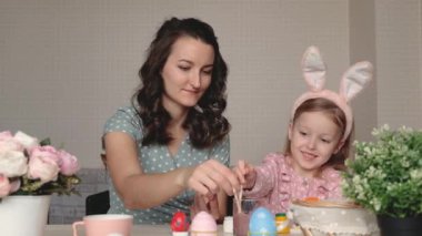 Paskalya, aile, tatil ve çocuk konsepti. Anne ve kızı yumurta boyuyor. Mutlu aile Paskalya için hazırlanıyor.