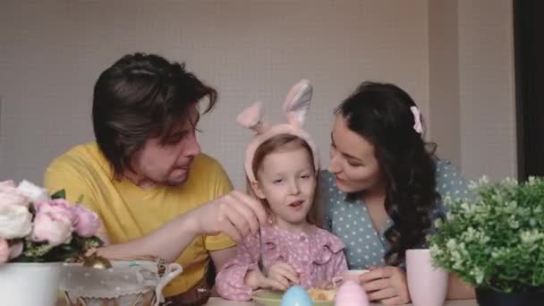 Happy Easter. Preparing family for Easter. Parents with child paints Easter eggs. Mother and father kissing daughter wearing bunny ears. Smiling faces. — Stock Video