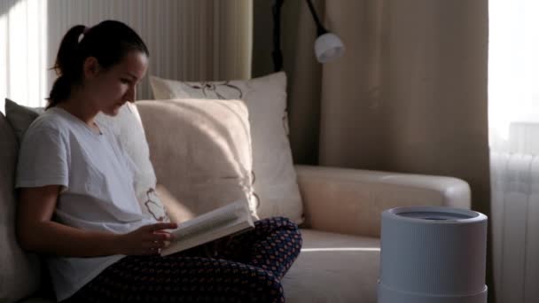 Humidificador de aire moderno, difusor de aceite de aroma en casa. Mejorar la comodidad de vivir en una casa, mejorar el bienestar. Tecnología de vapor ultrasónico. Mujer leyendo libro sobre fondo — Vídeo de stock