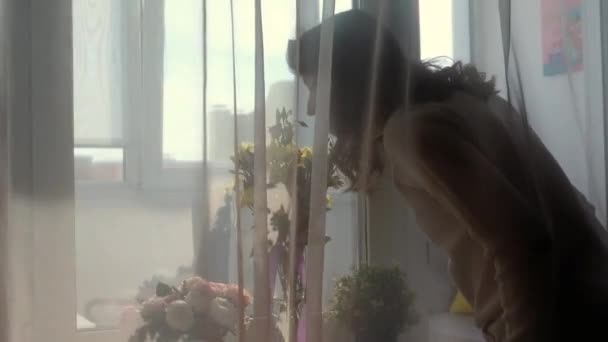 Jeune femme sentant les fleurs printanières dans un vase et regardant la fenêtre de la maison. Printemps d'été, concept de vie heureuse — Video