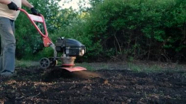Adam toprağı motorlu ekiciyle sürüyor. Traktörün arkasında, bahçede motor bloğu var. Yerleştirme hazırlığı.