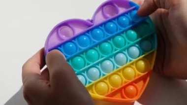 Eller stres önleyici, pop it oyuncağıyla oynar. Gökkuşağı duyusal kıpırdaması beyaz arka planda izole edilmiş. Yeni moda silikon oyuncak.