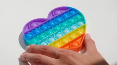 Eller stres önleyici, pop it oyuncağıyla oynar. Gökkuşağı duyusal kıpırdaması beyaz arka planda izole edilmiş. Yeni moda silikon oyuncak.