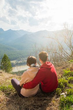 Genç gezgin çift dinleniyor ve dağlarda selfie çekiyor. Erkek ve kadın güzel kayalık bir patikada sırt çantalarıyla yürüyüş yapıyorlar. Aile seyahati ve macera konsepti