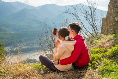 Genç gezgin çift dinleniyor ve dağlarda selfie çekiyor. Erkek ve kadın güzel kayalık bir patikada sırt çantalarıyla yürüyüş yapıyorlar. Aile seyahati ve macera konsepti