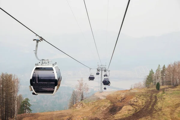 Lift cabins in a mountain ski resort. Ski lift ropeway on hilghland mountain winter resort on cloudy day. Ski chairlift cable way with people. Scenic panoramic wide view of downhill slopes. — Stock Photo, Image