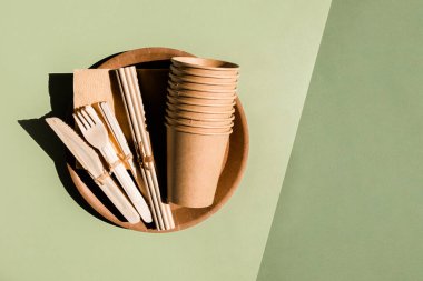 Ev için çevre dostu sofra takımı ve yeşil arka planda piknik. Plastiksiz. Sıfır atık. Tek kullanımlık kağıt sofra takımı, bardaklar, tabaklar, tahta çatallar, bıçaklar, kaşıklar ve bambu pipetler.