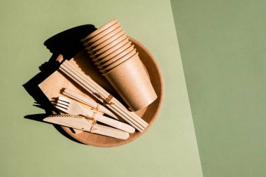 Ev için çevre dostu sofra takımı ve yeşil arka planda piknik. Plastiksiz. Sıfır atık. Tek kullanımlık kağıt sofra takımı, bardaklar, tabaklar, tahta çatallar, bıçaklar, kaşıklar ve bambu pipetler.