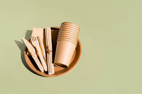 Set de vajilla ecológica para el hogar y picnic sobre fondo verde. Libre de plástico. Concepto de cero residuos. Vajilla de papel desechable, vasos, platos, tenedores de madera, cuchillos, cucharas y pajitas de bambú — Foto de Stock