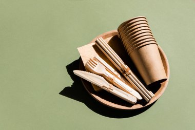 Ev için çevre dostu sofra takımı ve yeşil arka planda piknik. Plastiksiz. Sıfır atık. Tek kullanımlık kağıt sofra takımı, bardaklar, tabaklar, tahta çatallar, bıçaklar, kaşıklar ve bambu pipetler.