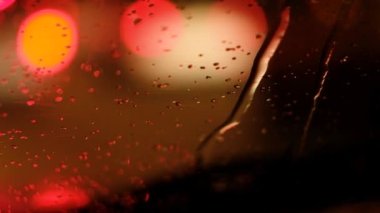 Pencere yüzeyine yağmur damlaları ve renkli trafik lambaları. Ön cama düşen yağmur damlaları. Yağmurlu bir günde araba sürmek.