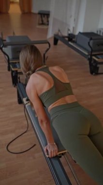 A young woman Snake practicing Pilates on a reformer machine in a gym setting. Fitness and health-focused exercise.