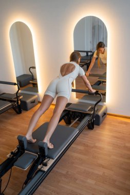 Bireysel pilates oturumu, kontrollü nefes alma ve titiz bir şekilde diz arkası gerilmesini gösteriyor.