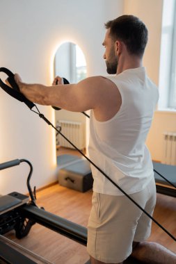 Eller yukarı, vücut kasları, vücut ve esnemeyi güçlendirmek için pilates yapan adam. Beden eğitimi egzersizlerini pilates makinesinde yapıyor. Pilates stüdyosunda egzersiz makinası. Yüksek kalite fotoğraf