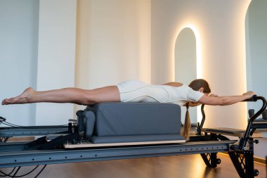 Aktif giyimli bir kadın güneşli bir stüdyoda göğüs ve sırt kasları için egzersiz yapıyor. Egzersiz yapmaya kendini adamış.