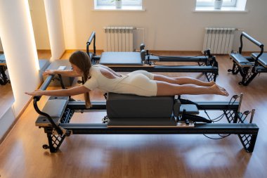 Aktif giyimli bir kadın güneşli bir stüdyoda göğüs ve sırt kasları için egzersiz yapıyor. Egzersiz yapmaya kendini adamış.