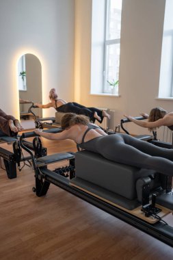 Beyaz bir kadın grubu parlak bir stüdyoda antrenörle pilates reformcuları üzerinde egzersiz yapıyor. Onların çalışmaları modern bir fitness ortamında çekirdek kuvveti ve esnekliği üzerine odaklanır. Yüksek kalite fotoğraf