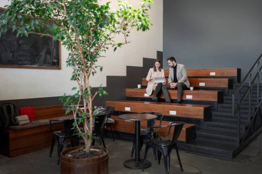 Takım, dekoratif bitkilerle dolu bir ofisteki ahşap koltuklar üzerinde çalışma kağıtlarını inceliyor. İnceleme, iş evrakları, takım çalışması, ofis, fabrikalar.