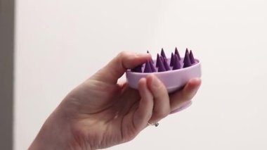 Kafa masajı ve saç bakımı için fırça. Bir kadının elindeki silikon kafa derisi masaj aleti. Bir kızın elinin parmaklarıyla silikon bir fırçanın kıllarını bükerken yakın çekimi. Kafa derisi masaj tarağı. Suç ortağı