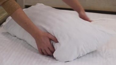 Yastığı kabartmak, yakın plan. Yastığı kabartan kadın elleri. Daire ya da otel temizliği konsepti. Sabah rutini. Kadın ellerinin rahat bir uyku için büyük bir yastığı kabartması.