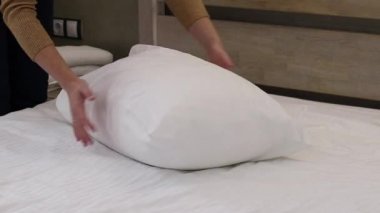 Yastığı kabartmak, yakın plan. Yastığı kabartan kadın elleri. Daire ya da otel temizliği konsepti. Sabah rutini. Kadın ellerinin rahat bir uyku için büyük bir yastığı kabartması.