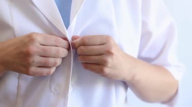 Doktor beyaz bir önlük giyer ve düğmeleri bağlar, yakın plan. Bir terapist önlüğü bağlar ve steteskopu alır. İş günü için bir doktor ya da hemşire hazırlıyorum. İlaç ve sağlık