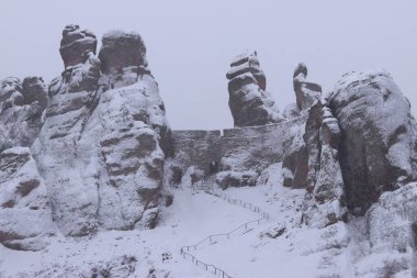 Karla kaplı Belogradchik kayaları. Bulgaristan. Kış havasında olağandışı şekillerde kaya oluşumları. Kar yağışı. Doğal dönüm noktası. Belogradchik şehri yakınlarındaki kayalar. Doğa