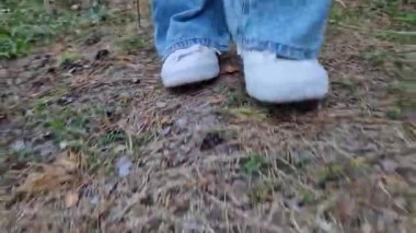 Ormanda yürüyorum. Ayaklar beyaz spor ayakkabılarda, zemin katı manzaralı. Parkta ya da ormanda yürürken. Ayaklara yakın çekim. Yazın dışarıda yürüyüş yapmak.