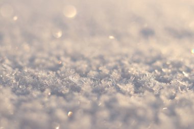 Seçici odaklı karlı bir arka plan. Yüzey karla kaplı, kar taneleri güneşte parlıyor. Karlı yüzey güneşte parlar, arka plan bulanıklaşır. Kış dönemi. Soğuk mevsim