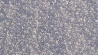 Karlı bir arka plan ve yakın plan kar taneleri. Yüzey karla kaplı, kar taneleri güneşte parlıyor. Karlı yüzey güneşte parlar. Kış dönemi. Soğuk mevsim