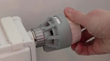 Bir kadının eli radyatörün termostatını çevirir. Bataryadaki ısı regülatörünün yakın çekimi. 0 ile 5 arasında derecelendirilmiş bir pil regülatörünün mekanik termal başı