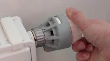 Bir kadının eli radyatörün termostatını çevirir. Bataryadaki ısı regülatörünün yakın çekimi. 0 ile 5 arasında derecelendirilmiş bir pil regülatörünün mekanik termal başı