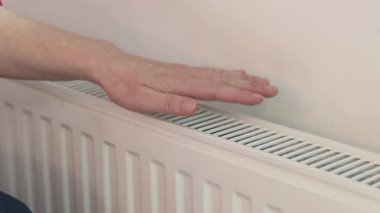 Evdeki radyatörün yanında ellerini ısıtan kadın. Donmuş ellerin yakın çekimi kendilerini radyatörün yanında ısıtıyor. Isıtma mevsimi, kışın odayı ısıtma. Ellerini ısıtan kız.