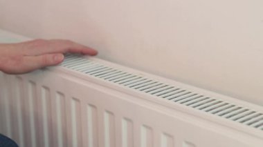 Evdeki radyatörün yanında ellerini ısıtan kadın. Donmuş ellerin yakın çekimi kendilerini radyatörün yanında ısıtıyor. Isıtma mevsimi, kışın odayı ısıtma. Ellerini ısıtan kız.