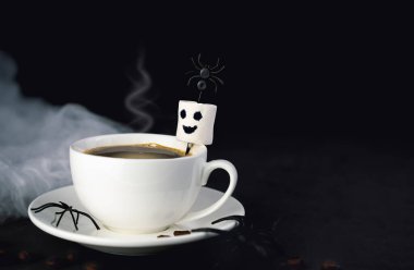 Sıcak kahve fincanı, gülümseyen marshmallow hayaleti ve koyu arkaplanda örümcekler. Şenlikli sabah kahvesi, Cadılar Bayramı ziyafeti ve sonbahar havası. Boşluğu kopyala.