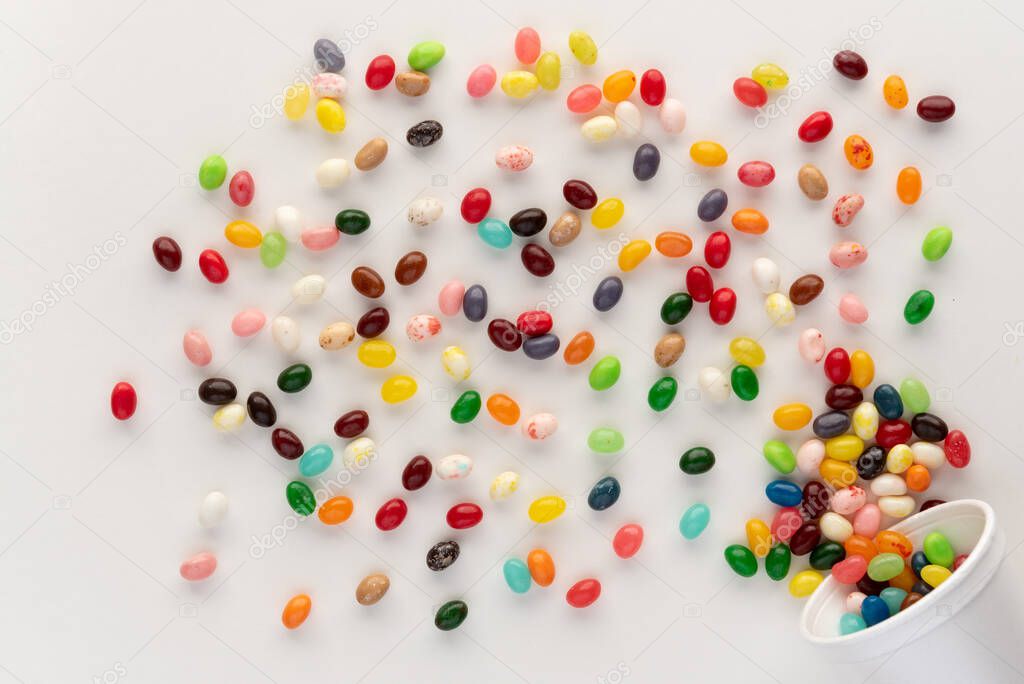  Jelly beans spilling from white foam cup against white background, festive and colorful composition with candie, overhead shot with a dynamic feel 