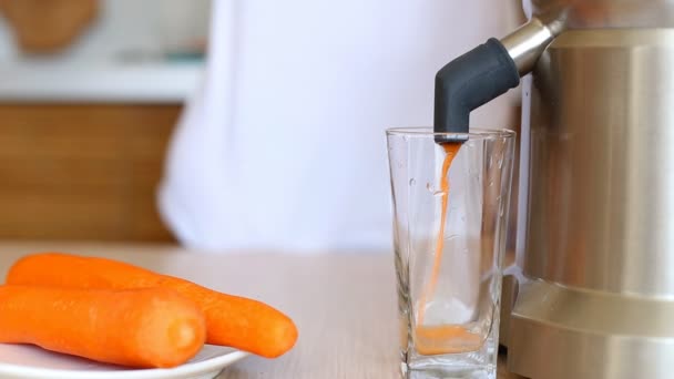 Świeży sok marchewkowy wlewa sokowirówki do szklanki na stole. — Wideo stockowe